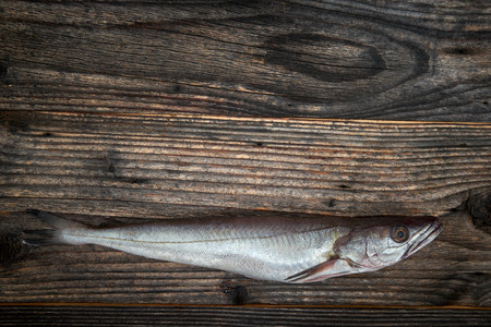 Raw fish (Merluccius) over wooden background, top view