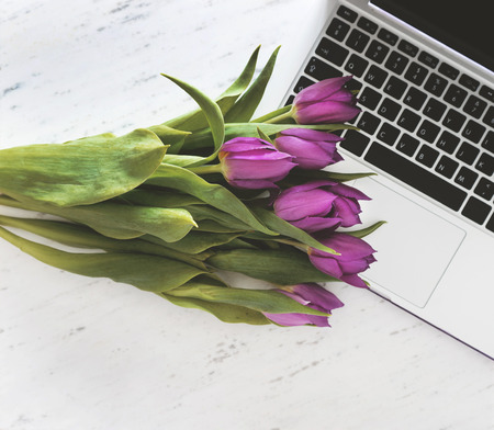 Computer with bouquet of purple tulips on marble background.の写真素材