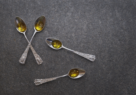 Olive oil in vintage spoons on black marbleの写真素材