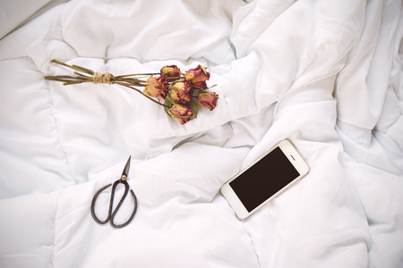 Dry roses, smartphone and vintage scissors on bed, top viewの写真素材