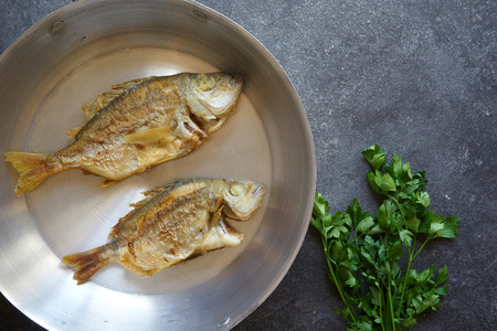 Fried fish in an old pan on the table, top viewの写真素材