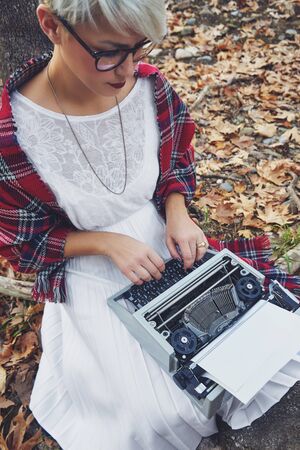 Vintage concept with a young woman sitting in the tree and typing on a typewriter