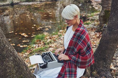 Vintage concept with a young woman sitting in the tree and typing on a typewriterの写真素材