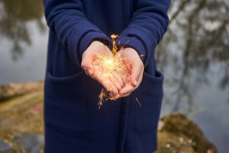 Woman holding sparkler in forest, winter day