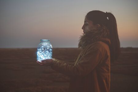 Girl is holding fairy lights in a jar on winter dry landscapeの写真素材