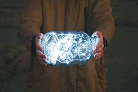 Girl is holding fairy lights in a jar on winter dry landscapeの写真素材
