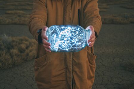 Girl is holding fairy lights in a jar on winter dry landscapeの写真素材