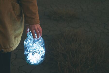 Girl is holding fairy lights in a jar on winter dry landscapeの写真素材