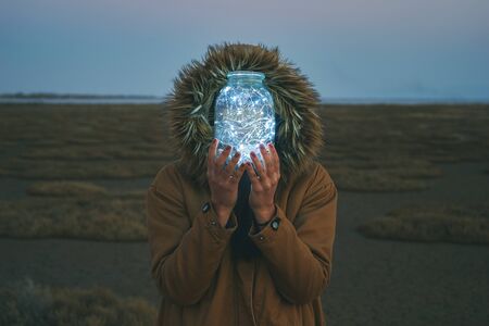 Girl is holding fairy lights in a jar on winter dry landscapeの写真素材
