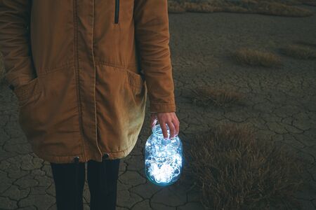 Girl is holding fairy lights in a jar on winter dry landscapeの写真素材