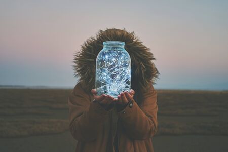 Girl is holding fairy lights in a jar on winter dry landscapeの写真素材