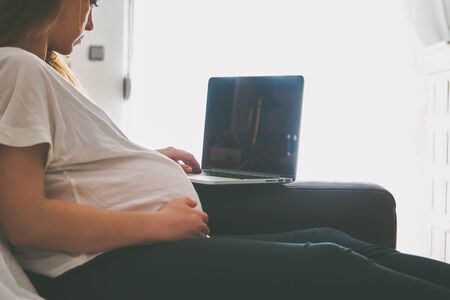 Young pregnant woman relaxing on sofa with laptopの写真素材