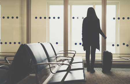 Young woman in the airport, looking through the window at planesの写真素材