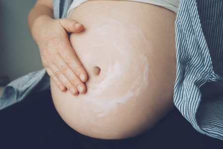 Pregnant woman putting cream on her belly to avoid stretch marksの写真素材