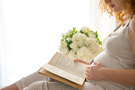 Pregnant woman touching her belly while she is readind a bookの写真素材