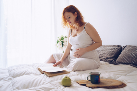 Young pregnant woman relaxing on the bed with a bookの写真素材