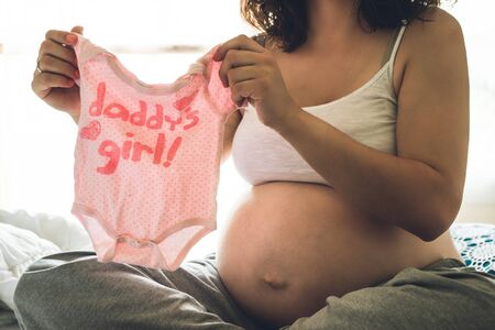Happy pregnant woman holding baby clothingの写真素材