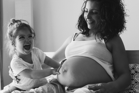 Happy kid girl with her pregnant mother on the bedの写真素材
