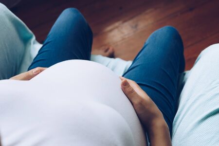 Close up of young pregnant woman touching her belly, top view
