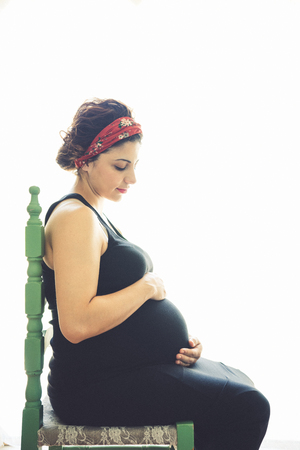 Pretty young pregnant woman sitting by the window in roomの写真素材