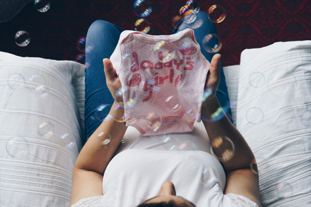 Pregnant woman holding baby clothes in her hands, top viewの写真素材