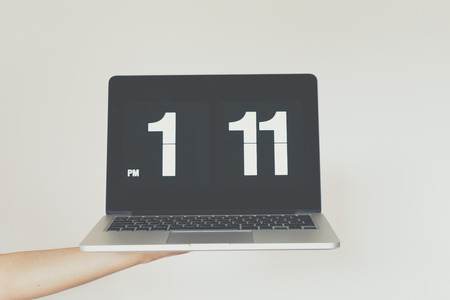 Womans hand  holding computer with clock front of white background.の写真素材