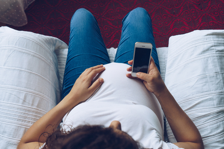 Pregnant woman holding smartphone in her hands, top viewの写真素材
