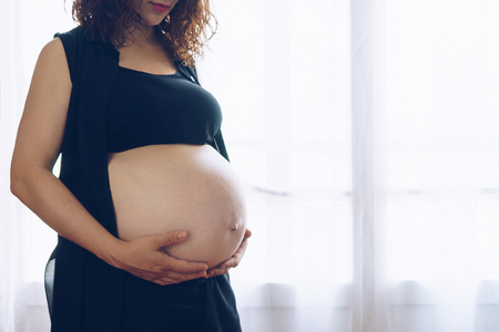 Pregnant woman standing against the windowの写真素材