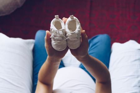 Pregnant woman holding baby shoes  in her hands, top viewの写真素材