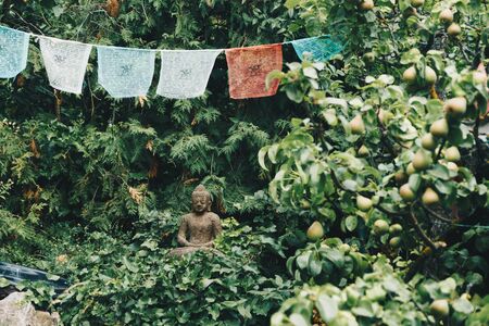 Buddha sculpture on green nature and buddhist prayer flagsの写真素材
