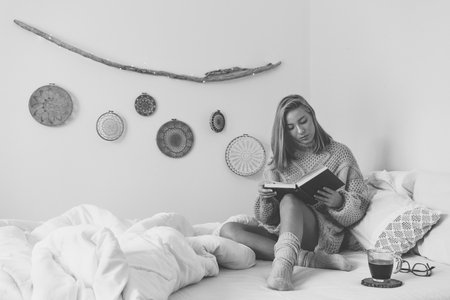 Young woman sitting in bed while reading a bookの写真素材