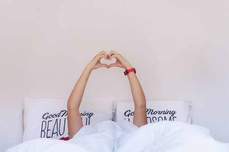 Girl making a heart-shape with her hands under the blanket on the bed