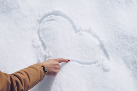 Woman is drawing a heart on the snow