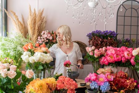 Beautiful blonde florist woman picks up flowers and creates wonderful bouquetの写真素材