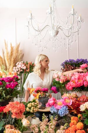 Beautiful blonde florist woman picks up flowers and creates wonderful bouquetの写真素材