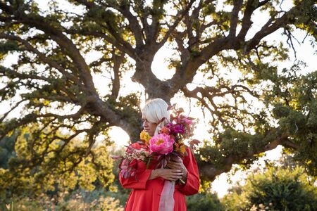 Beautiful young woman with flowers in the field and a tree as a backgroundの写真素材