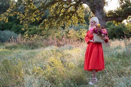 Beautiful young woman with flowers in the field and a tree as a backgroundの写真素材