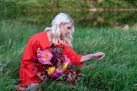 Beautiful young woman with flowers in the field and a lake as a backgroundの写真素材
