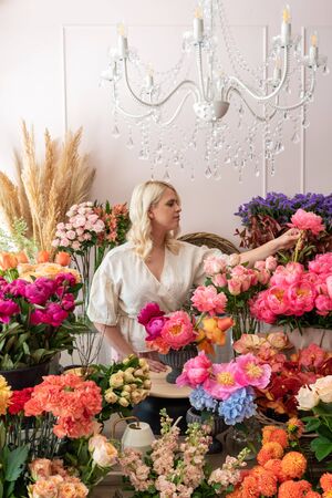 Beautiful blonde florist woman picks up flowers and creates wonderful bouquetの写真素材