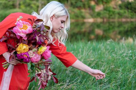 Beautiful young woman with flowers in the field and a lake as a backgroundの写真素材