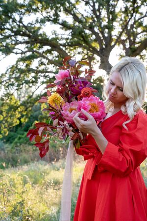 Beautiful young woman with flowers in the field and a tree as a backgroundの写真素材