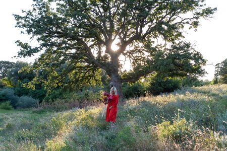 Beautiful young woman with flowers in the field and a tree as a backgroundの写真素材