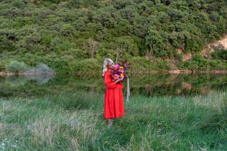 Beautiful young woman with flowers in the field and a lake as a backgroundの写真素材