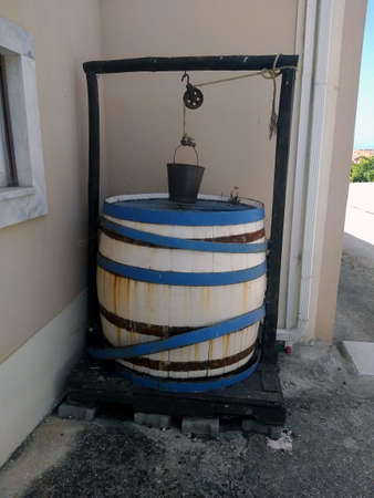 Antique painted wooden barrel-well with an old bucket in the courtyard of a rural houseの写真素材