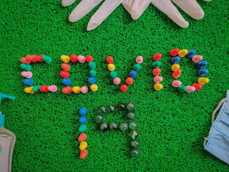 Inscription Covid-19 text made with game board pieces. Medical gloves, mask, sanitizers. Isolated on green background. Medical conceptの写真素材