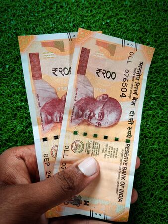 Hand holding of two two hundred rupees notes. Isolated on green background. Daylight.の写真素材