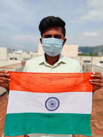 South Indian man wearing face mask holding or showing Indian flag in his hands. Happy Independence...