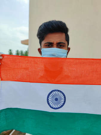 South Indian man wearing face mask holding or showing Indian flag in his hands. Happy Independence day India. Outdoors. Daylight,の写真素材