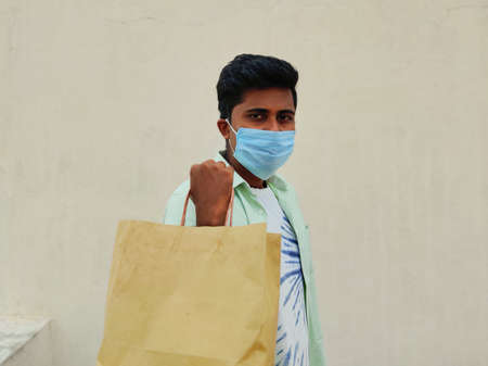 Young South Indian wearing mask is holding shopping bag. Isolated on white background. Shopping...