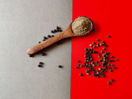 Wooden spoon filled with pepper powder surrounded with some pepper seeds. Isolated on grey and red background.の写真素材